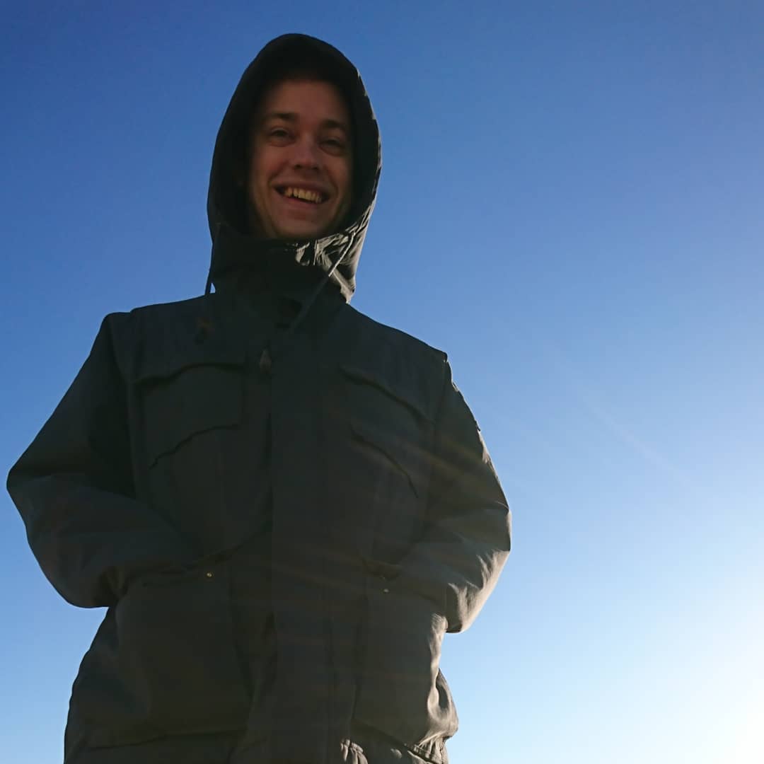 An image of Kevin wearing a jacket with the sun and blue sky behind him